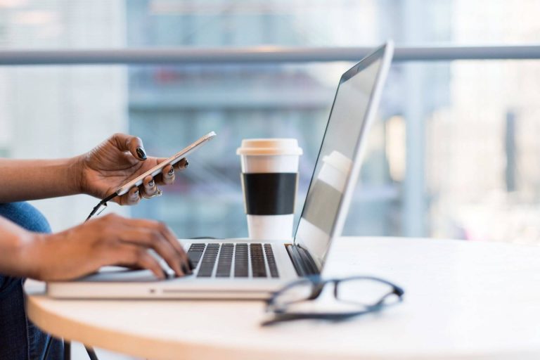 person using smartphone and MacBook to research ways small businesses save money with cloud communications